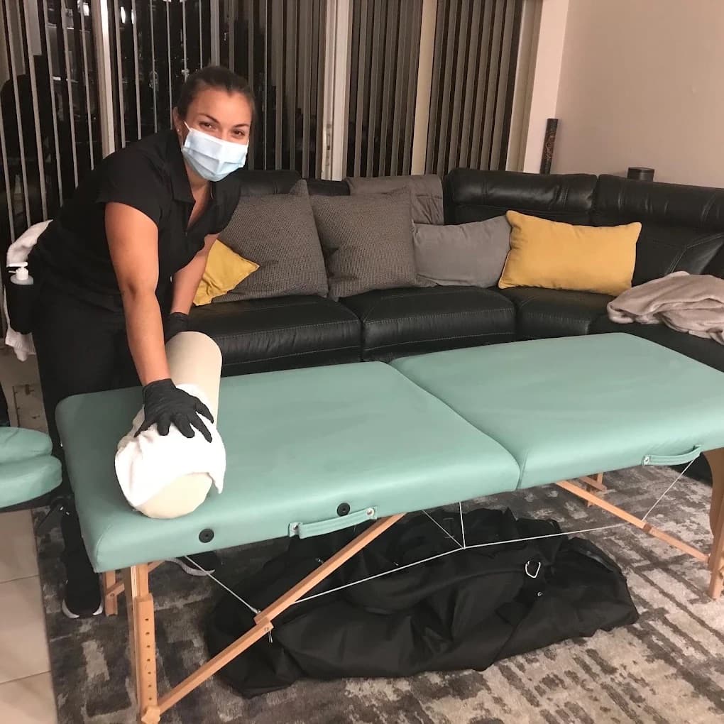 Yeslie Valdes, masked and gloved, setting up a portable massage table in a client's living room during the COVID-19 pandemic
