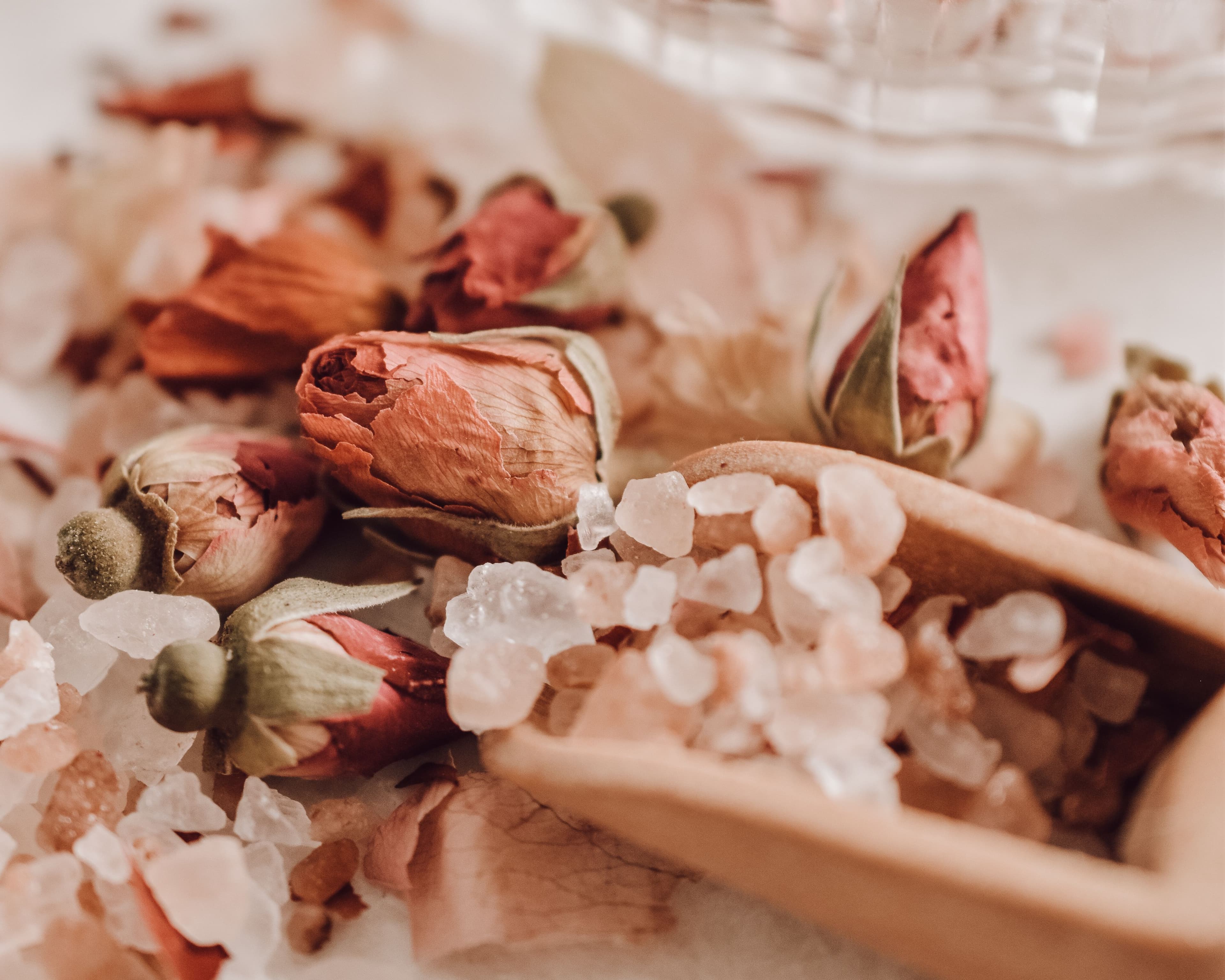 Dried rose buds and pink mineral salt in a wooden scoop